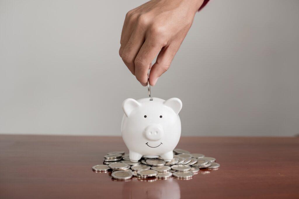 The hand of a businessman puts coins in a piggy bank, saves money with coins, steps into